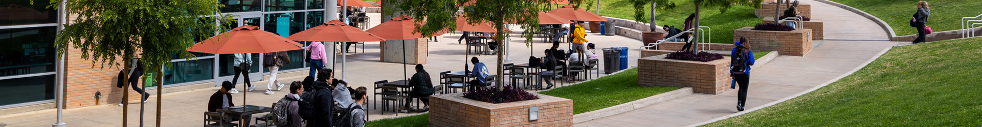 Students at tables shaded by orange umbrellas in the outdoor plaza next to the Highlander Union Building at UC Riverside.