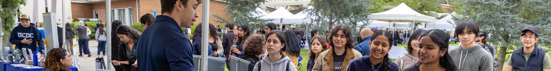 Prospective students and families talk with a representative at an outdoor university information fair.