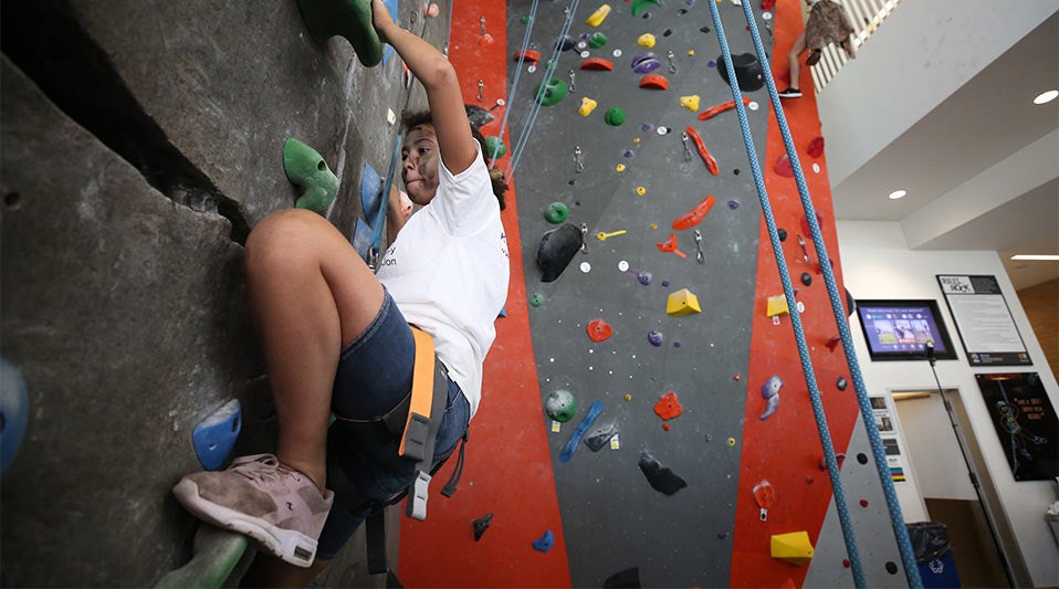 A young male student is scaling at rock wall at the SRC