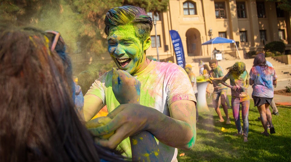 A color festival is in full swing in front of Anderson Hall. Smiling students are covered in multi-colored dust.