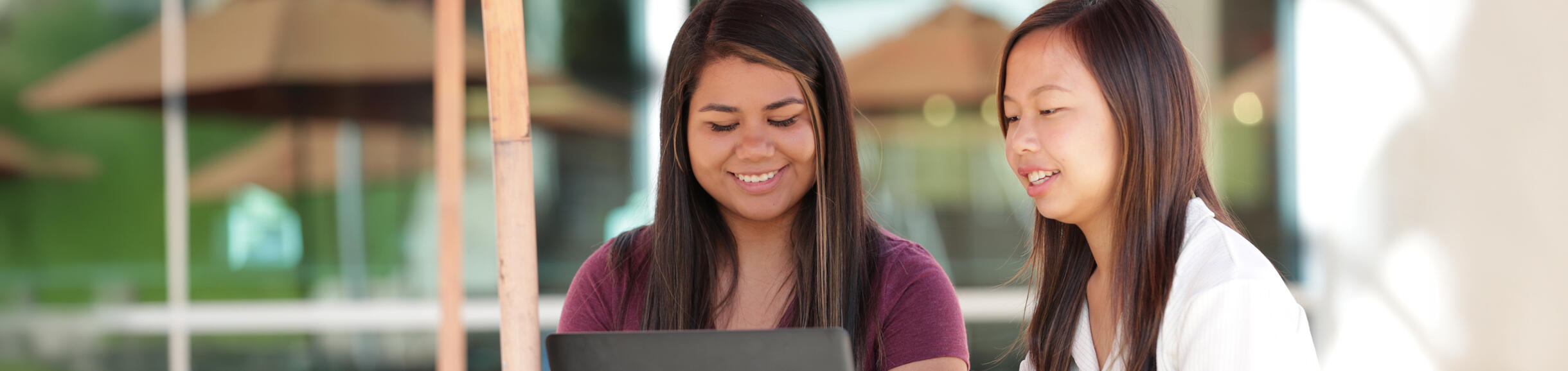 Two UC Riverside students study together on a laptop on a sunny outdoor patio.