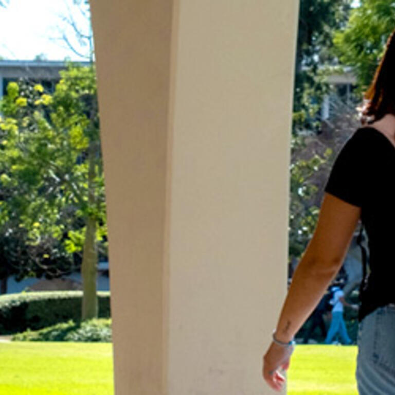 Students walk near the Tomás Rivera Library at UC Riverside, with a student carrying a backpack in the foreground.