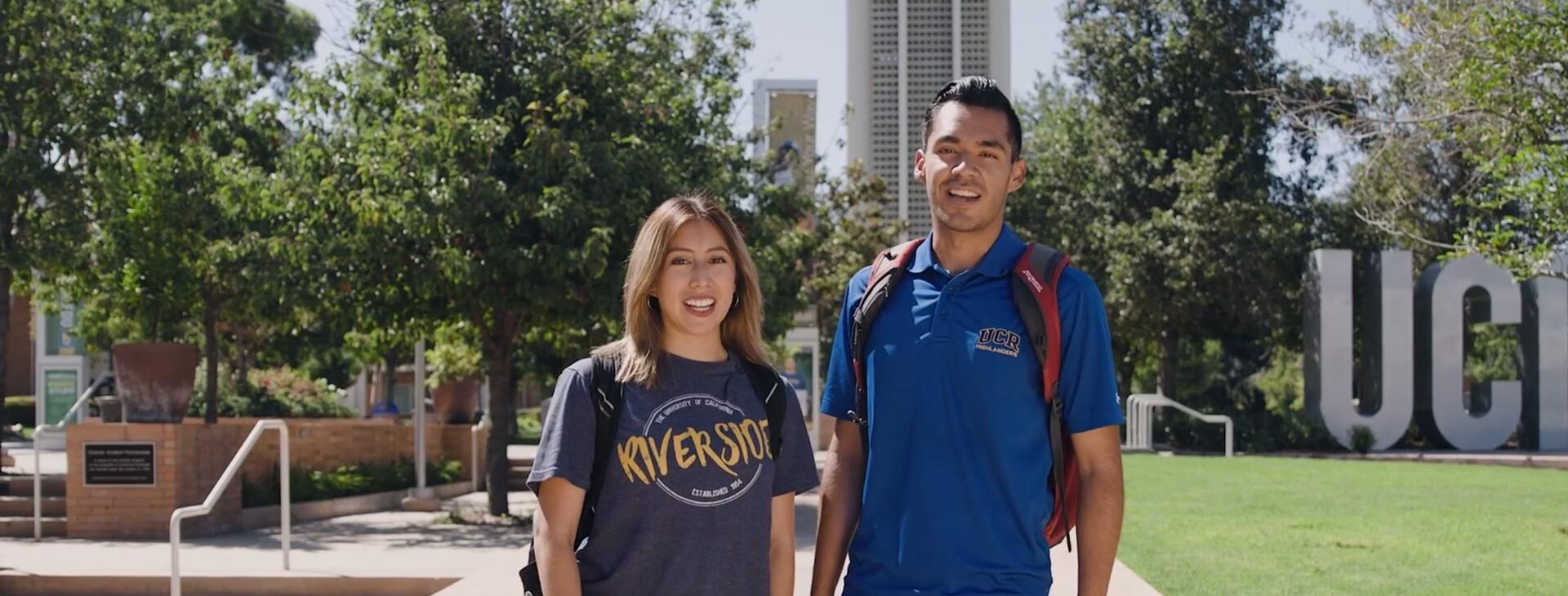 Two UCR students stand on campus near the Bell Tower, ready to give a tour on how to apply to UC Riverside.