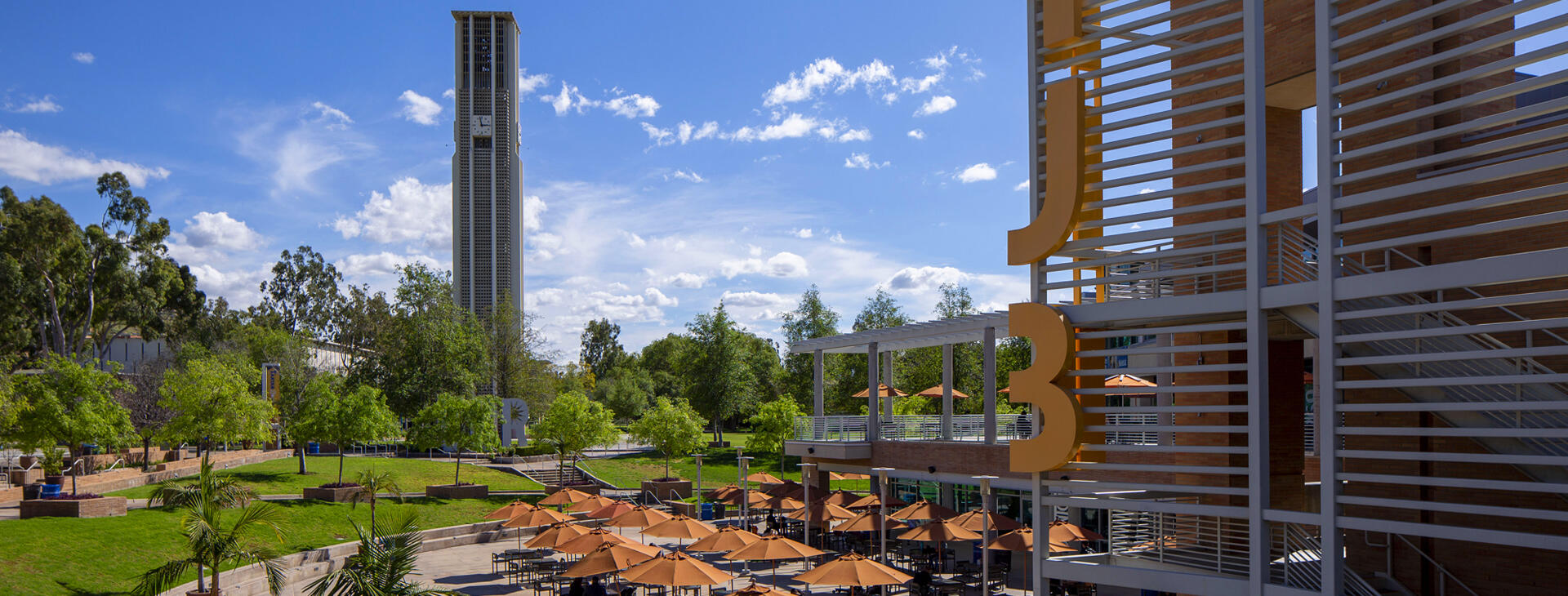 The UCR Bell Tower on a sunny day, overlooking an outdoor plaza with students studying under many orange umbrellas.